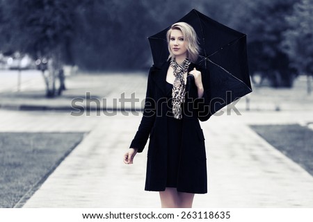 Happy young fashion woman with umbrella walking in the rain