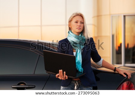 Young fashion business woman with laptop by her car