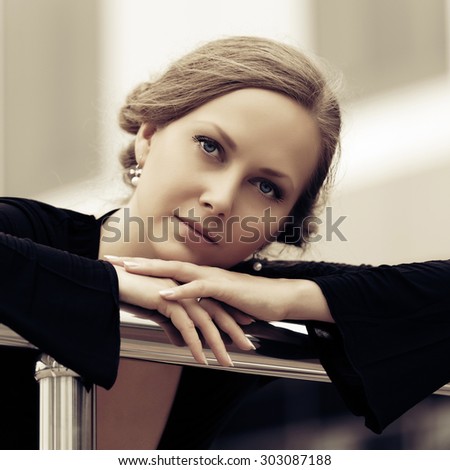 Sad beautiful fashion woman in black dress leaning on handrail