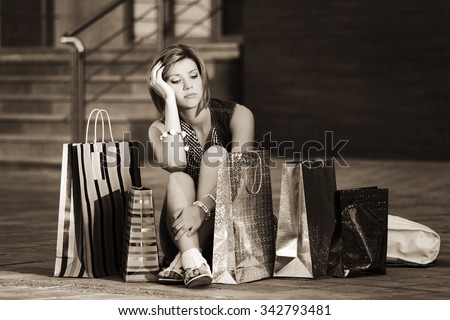 Sad young fashion woman with shopping bags sitting on a sidewalk