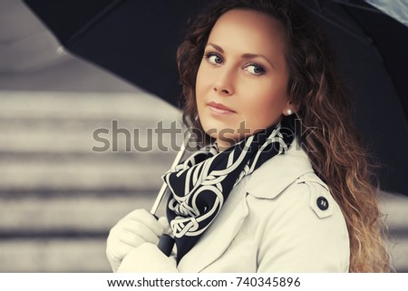 Beautiful fashion woman in white trench coat walking in city street. Stylish female model with umbrella outdoor