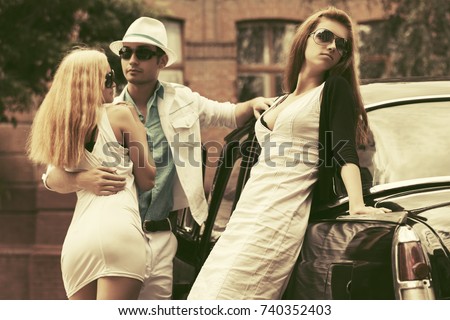 Young fashion man and women next to retro car in city street. Stylish male and female models outdoor