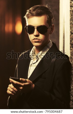 Young handsome business man using smartphone in a night city street. Stylish fashion male model in black blazer outdoor