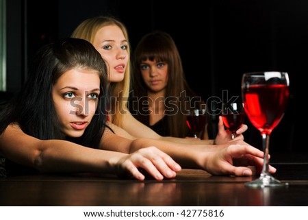 Three young women drinking red wine in a bar.