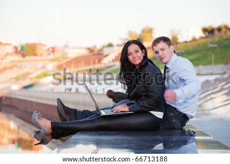 Young couple with laptop on the river embankment.