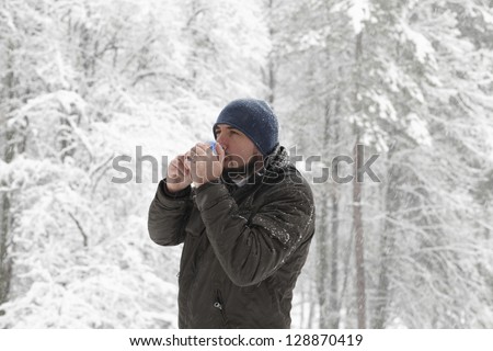 Winter man portrait - Young good looking men is holding a cup of tea and drinking it. Photo is taken outside in a cold snowy forest.