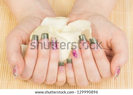 Manicure - Beauty treatment photo of nice manicured woman fingernails holding the flower. Very interesting nail art with glitter green, purple and pink nail polish.