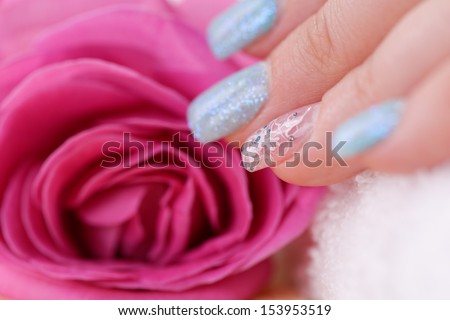 Manicure - Beautiful manicured woman\'s fingernails with glitter blue nail polish and nail art on fourth finger touching rose. Studio shot. Selective focus.