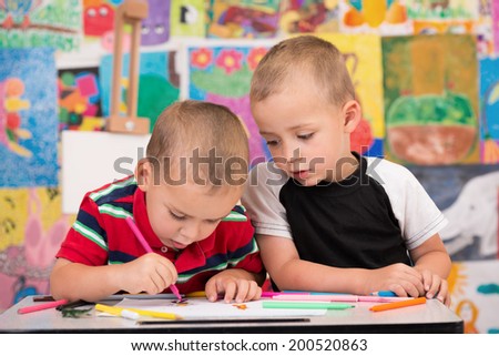 Two cute little boys drawing using felt-tip pen and colorful pencils while sitting at table.