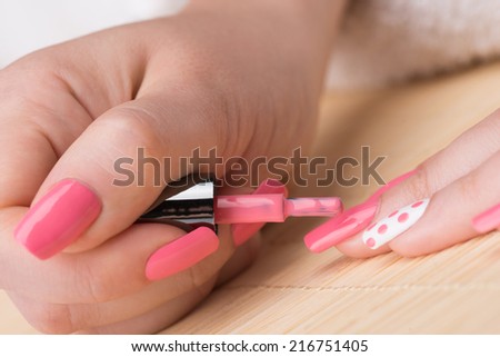 Manicure - Beauty treatment photo of nice manicured woman fingernails. Feminine nail art with nice pink and white nail polish. Selective focus on nail polish brush.