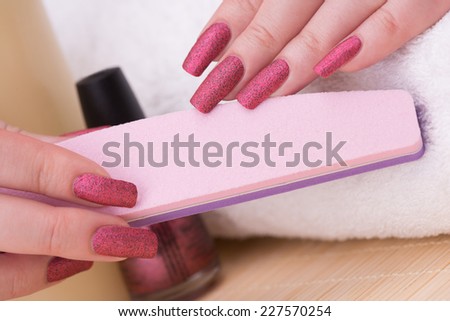 Manicure - Beauty treatment photo of nice manicured woman fingernails holding nail file. Textured reddish polish filled with tiny black glitters that dries to a matte satin finish.