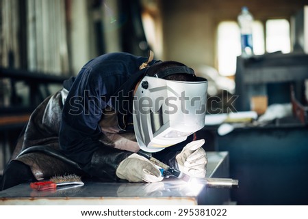 Welder at work using welding mask, tools and machinery on metal. Selective focus.