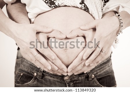 happy pregnant woman on white background with crossed arms and hands of the father a heart-shaped on the belly