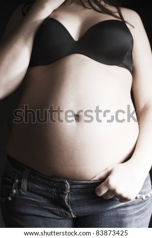 big belly pregnant woman in jeans and black bra on a black background