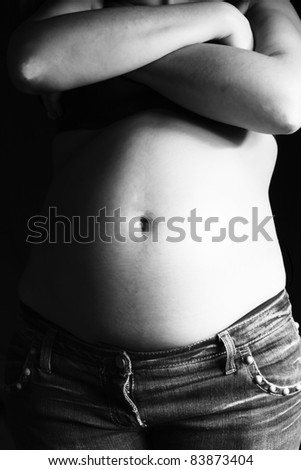 big belly pregnant woman in jeans and black bra on a black background with crossed arms