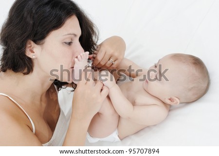 Mother is kissing her baby feet while play on a white bed