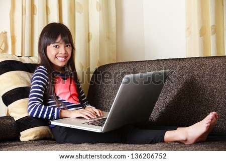 Little asian girl  with computer at home laying on sofa