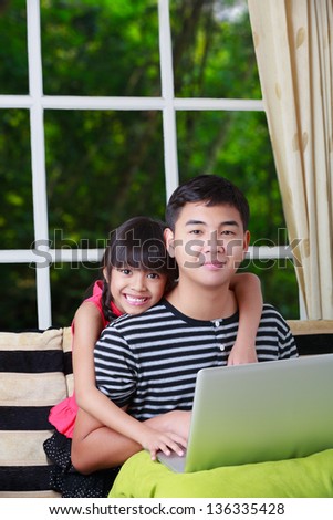 Little asian girl pointing on laptop with big brother at home