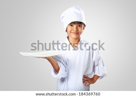 Little asian girl chef showing the empty white plate, Isolated on grey