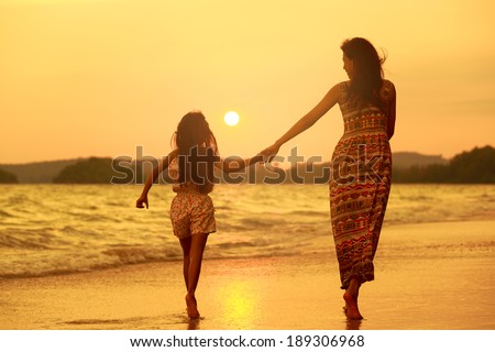Mother and daughter walking on the beach with sunset Mother and daughter walking on the beach with sunset