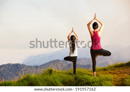 Mother and daughter doing yoga at top of mountain