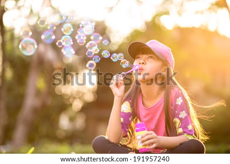 Little asian girl blowing soap bubbles outdoor at sunset Little asian girl blowing soap bubbles outdoor at sunset