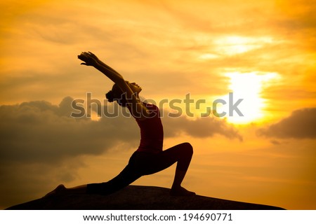 Young asian woman practicing yoga warrior pose at sunset