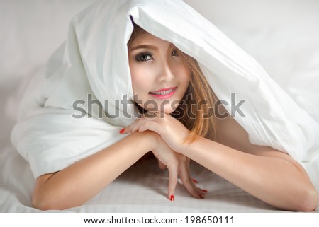 Smiling young asian woman in bed under white blanket