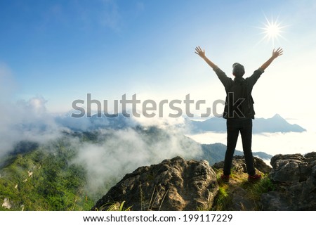 Teenager boy with backpack standing on top of a mountain with raised hands