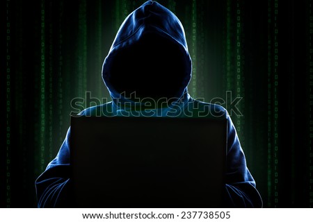 Faceless hooded anonymous computer hacker with programming digital code from monitor