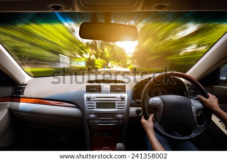 Hands on steering wheel of a car and motion blurred asphalt road and sky Hands on steering wheel of a car and motion blurred asphalt road and sky