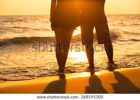 Couple legs silhouette falling in love at sunset on the beach with the sun in the background