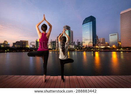 Mother and daughter doing yoga tree pose at city