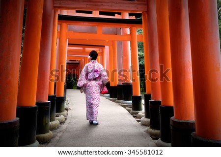 Woman dressed in traditional japanese costume walking under tori gates at the fushimi-inari shrine, Kyoto Japan