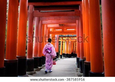 Woman dressed in traditional japanese costume walking under tori gates at the fushimi-inari shrine, Kyoto Japan