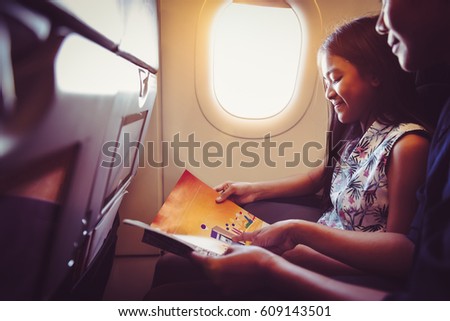 Mother with daughter sit on their place in airplane economy class and read a magazine