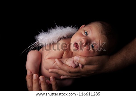 Smiling peaceful newborn baby boy with angel wings in father\'s hands. Studio shot, over black background with copy space.
