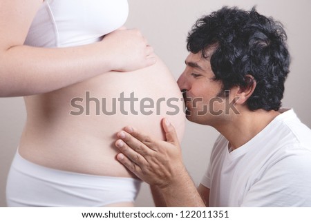 Father kissing pregnant belly of wife. Concept of love, over white background.