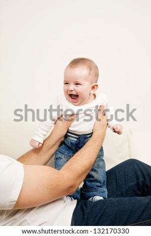 Adorable laughing baby boy standing on fathers laps with support