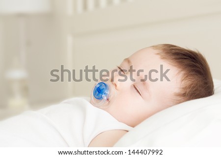 Adorable sleeping baby on the pillow with pacifier and bottle of milk at the background