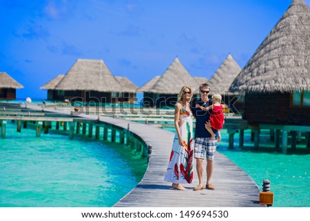 Family of three walking on the bridge towards to water bungalows on Maldives