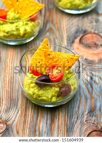 Guacamole with avocado decorated with olives, tomato and tortilla chips.