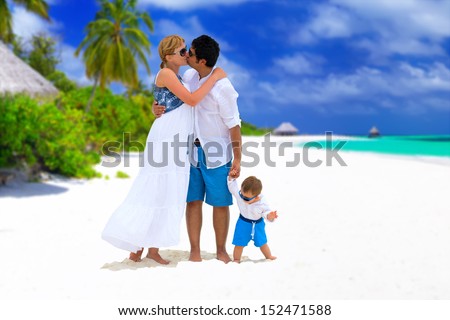 Happy family of three having tropical vacation on Maldives. Parents with baby kissing on the beach.