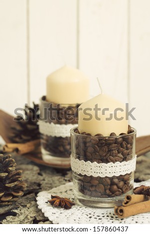 Two candles with natural ornaments in glass on a wooden background. Handmade decoration for Christmas from coffee beans - ideas for holidays gifts.