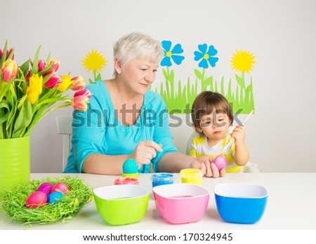 Loving grandma teaching her grandson to color eggs for Easter at home