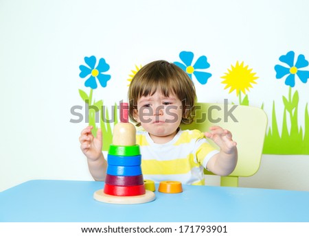Frustrated baby learning how to build pyramid toy in kindergarten or day care, intellectual development