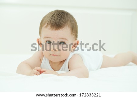 Portrait of cute baby in bed, lying on his belly and looking at the camera