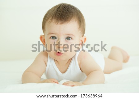 Portrait of cute baby in bed, lying on his belly and looking at the camera with interest. Indoors shot.