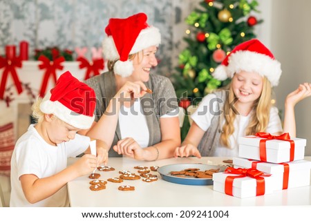 Happy family of three decorating Christmas cookies, having fun at home, with Christmas Tree and chimney