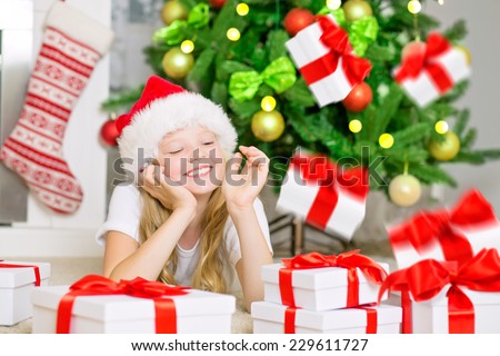 Happy girl with radiant face, smiling and enjoying christmas gift\'s fall. Little girl with Santa Hat , Christmas gifts boxes under illuminated Christmas Tree and chimney. Christmas card.
